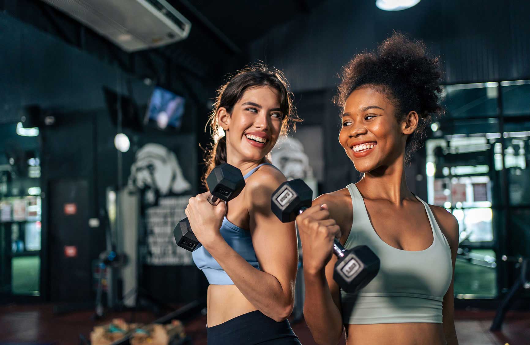 Latino and African sport woman exercising and build muscle in stadium. Active strong beautiful fit athlete girls in sportswear workout lifting weight dumbbell for arm and health care at fitness club.