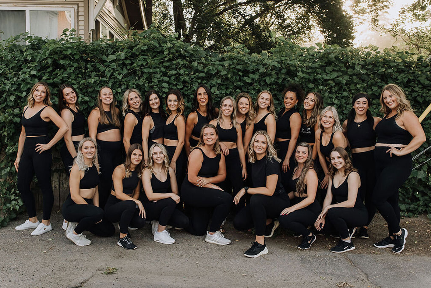 a large group of women posing infront of a bush thwy ar all wearing black