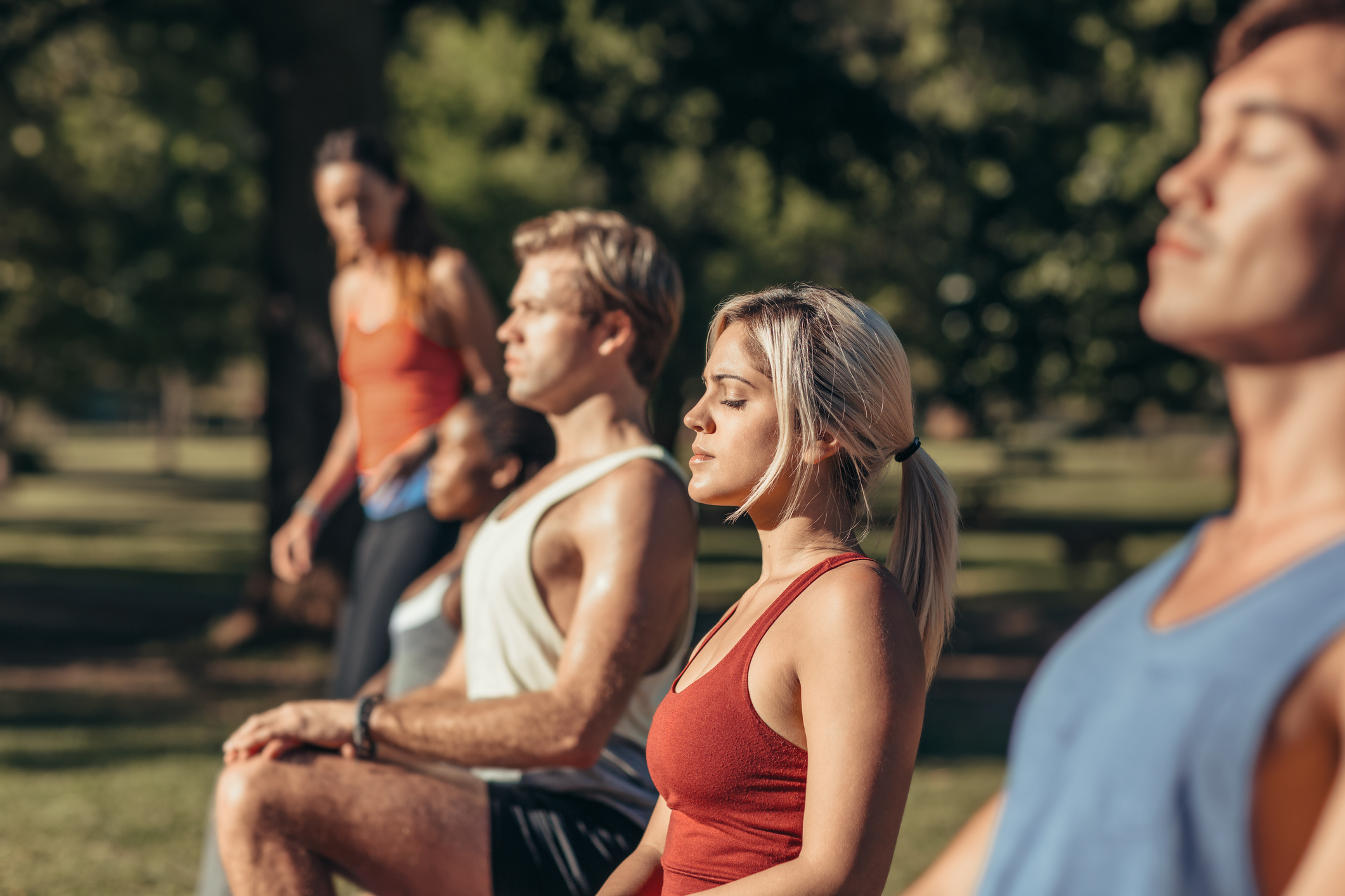 Group of fit young people in sportswear stretching while doing yoga together in a park on a sunny day