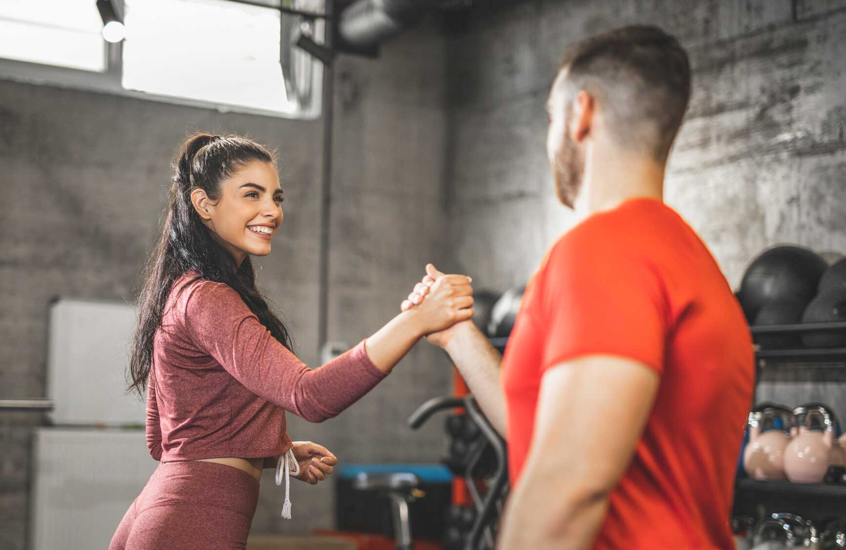 Young woman and man are shaking hands after an intense training in the gym. Focus on woman