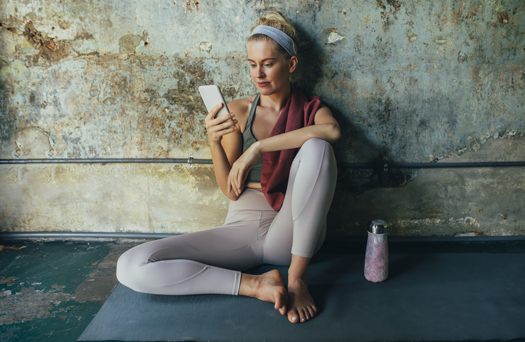 A beautiful blonde woman resting on a mat after doing yoga and scrolling through her smartphone