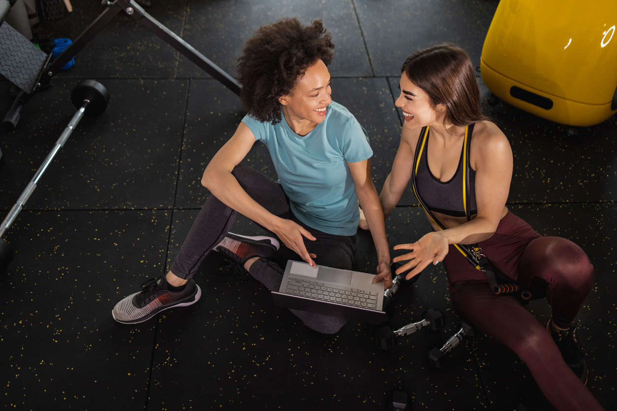 High angle view of two female friends in the gym, taking a break and looking at laptop