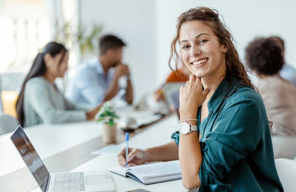 Female Employee Smiling in the Office, With Her Colleagues in Background. Shallow Focus