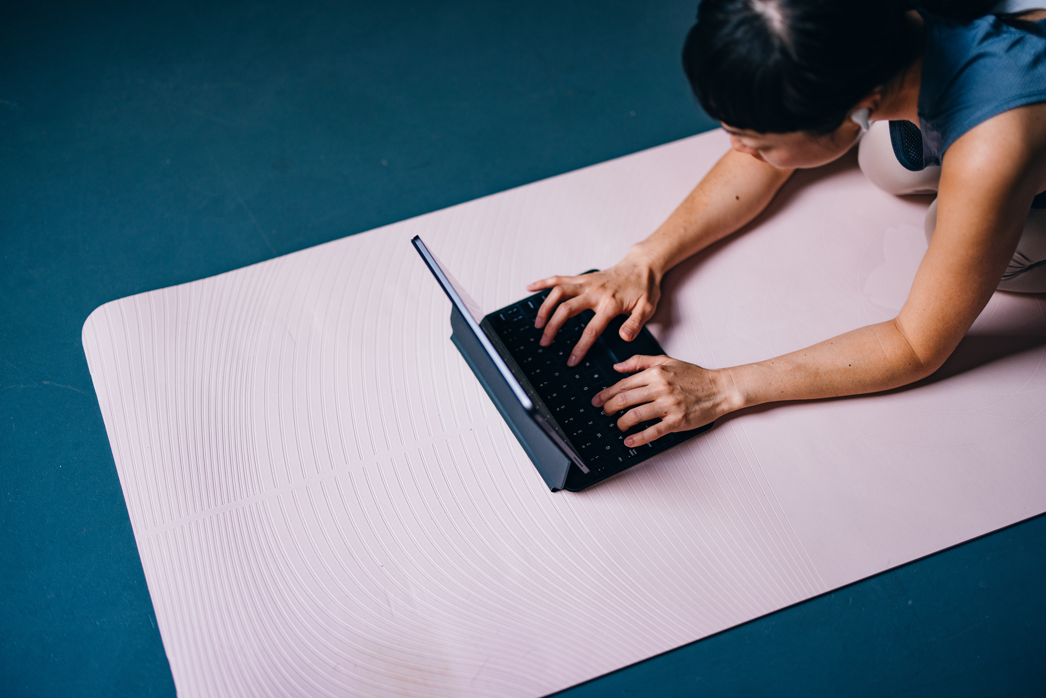 High angle view of an anonymous Asian woman woman in sportswear kneeling on a exercise mat and searching for a training videos online on her tablet.