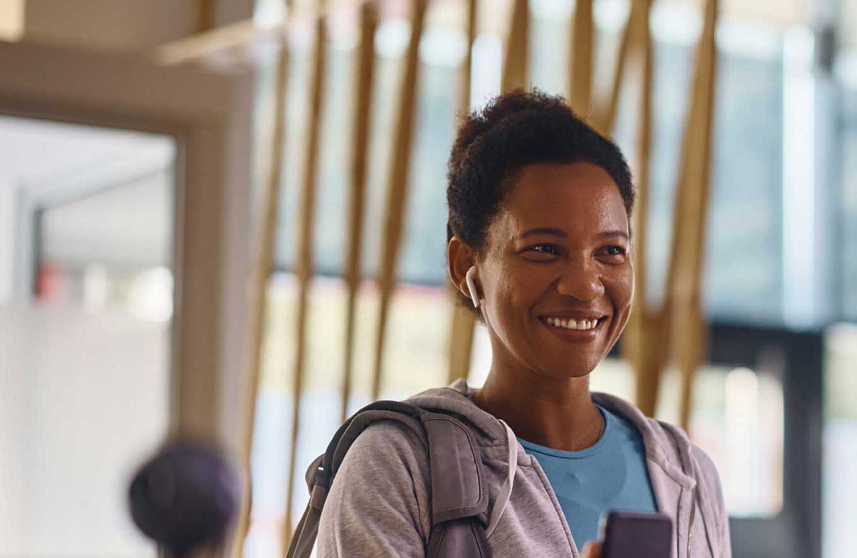 Happy African American athletic woman checking in with cell phone at reception deskin a gym.