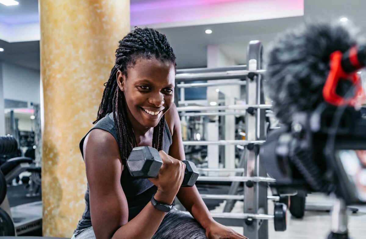 Beautiful young black fitness vlogger filming a workout routine in the gym.