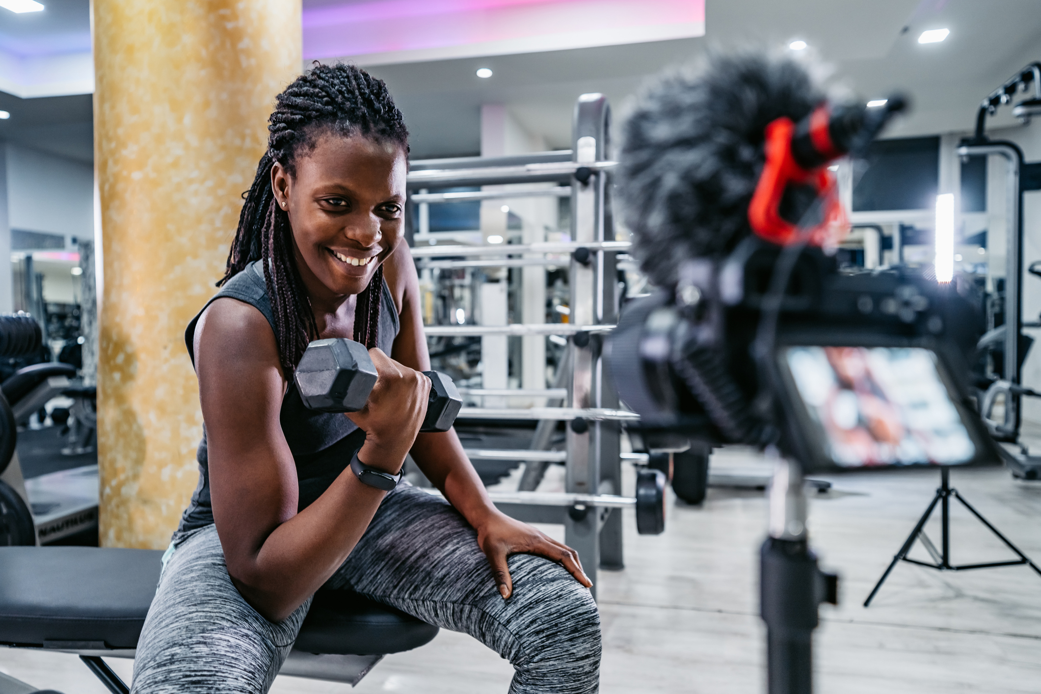 Beautiful young black fitness vlogger filming a workout routine in the gym.