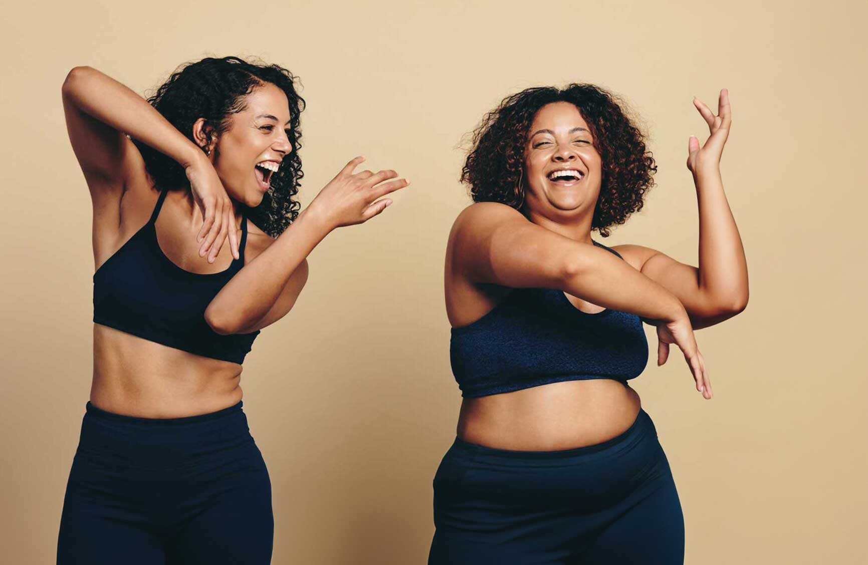 Two young women, wearing sports clothing and full of vitality, dance and exercise together in a studio. Happy female athletes having fun and celebrating their fit lifestyle.