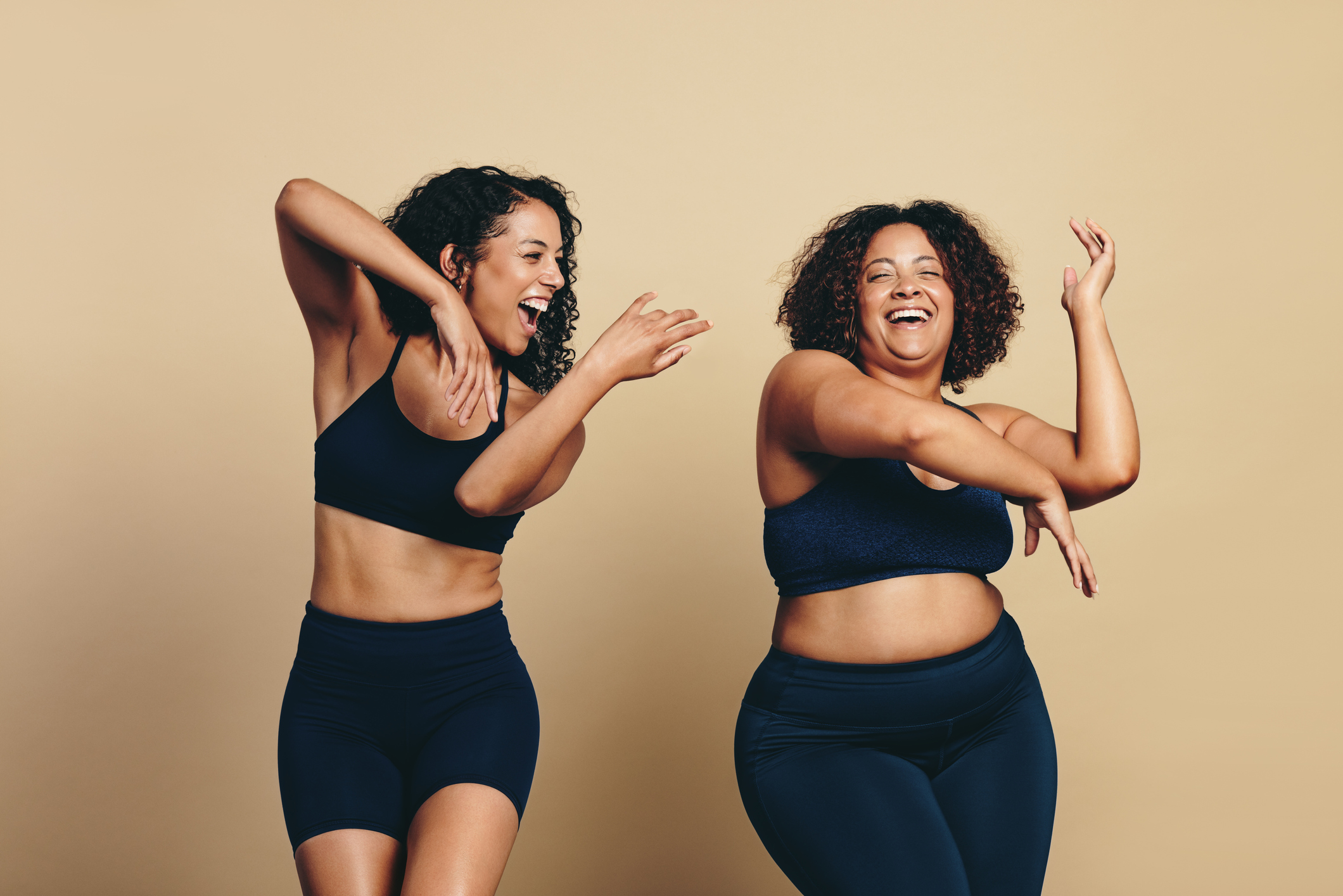 Two young women, wearing sports clothing and full of vitality, dance and exercise together in a studio. Happy female athletes having fun and celebrating their fit lifestyle.