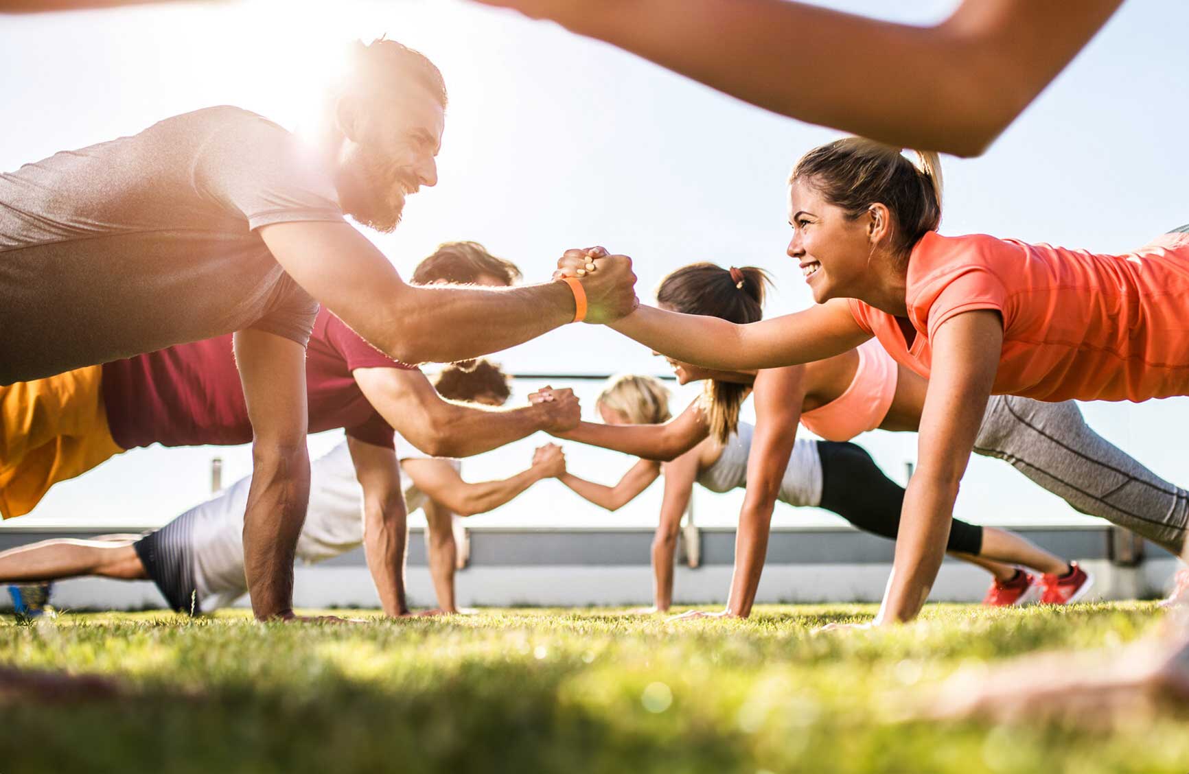 Low angle view of athletes cooperating while exercising on a sports training outdoors. Focus is happy couple.