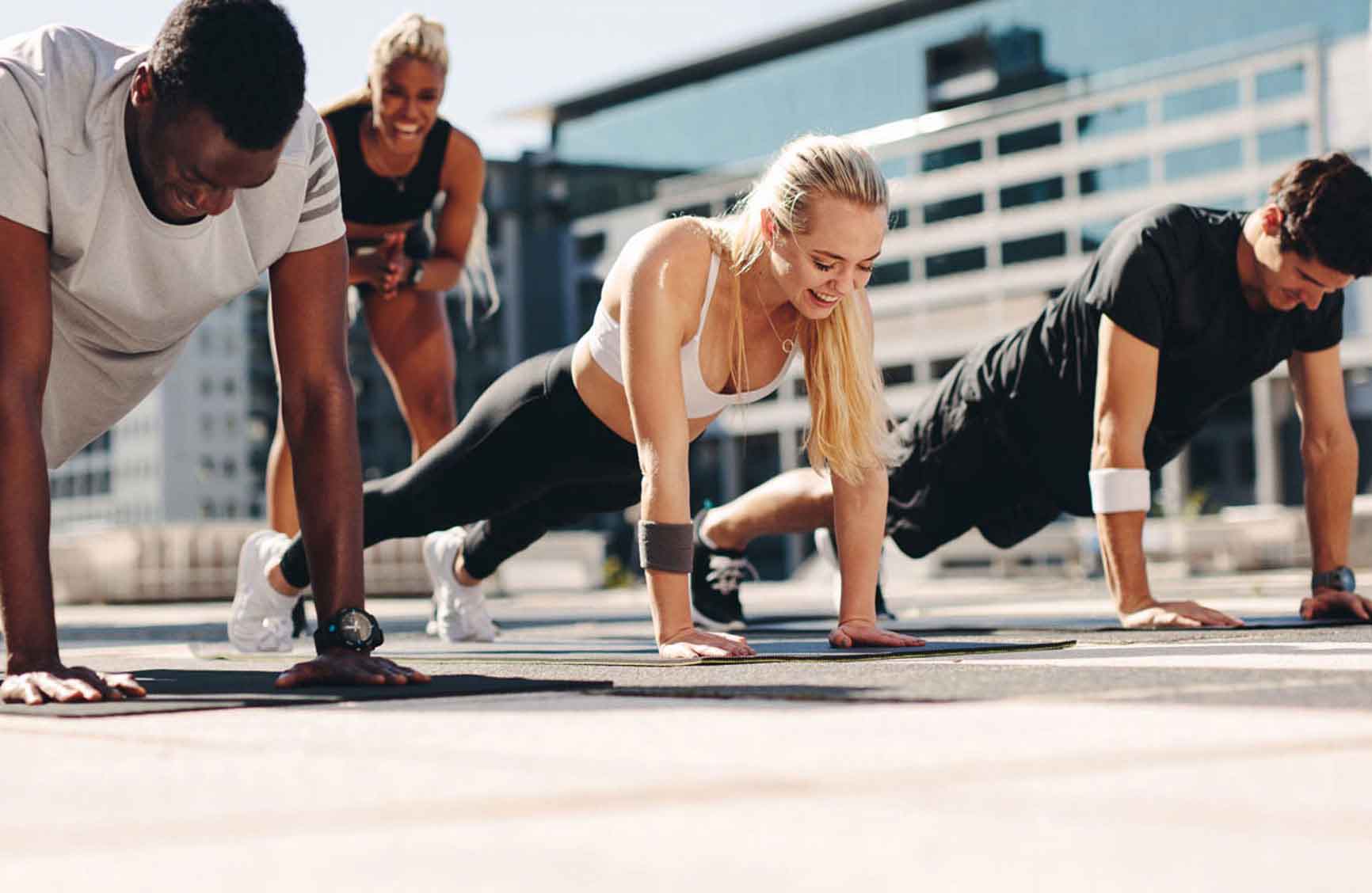 Fitness men and women doing push-ups with motivation from their female trainer outdoors in the city.