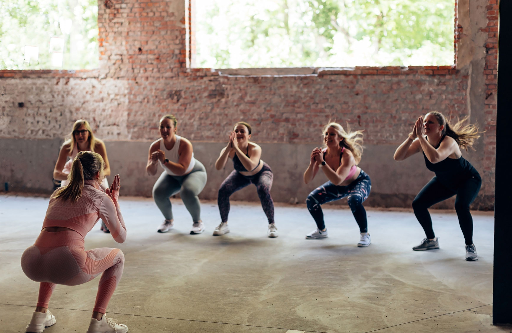 rear view of a personal trainer giving gymnastics class to a group of women with different body shapes - jumping squat hiit workout