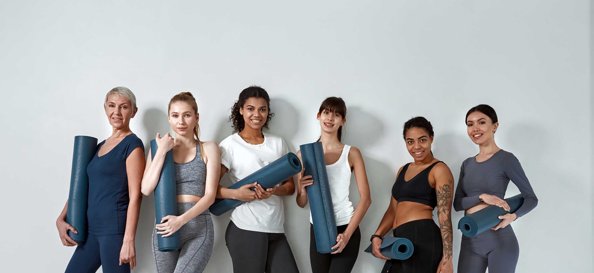 a group of multi-cultural ladies looking at the camera while holding yoga mats